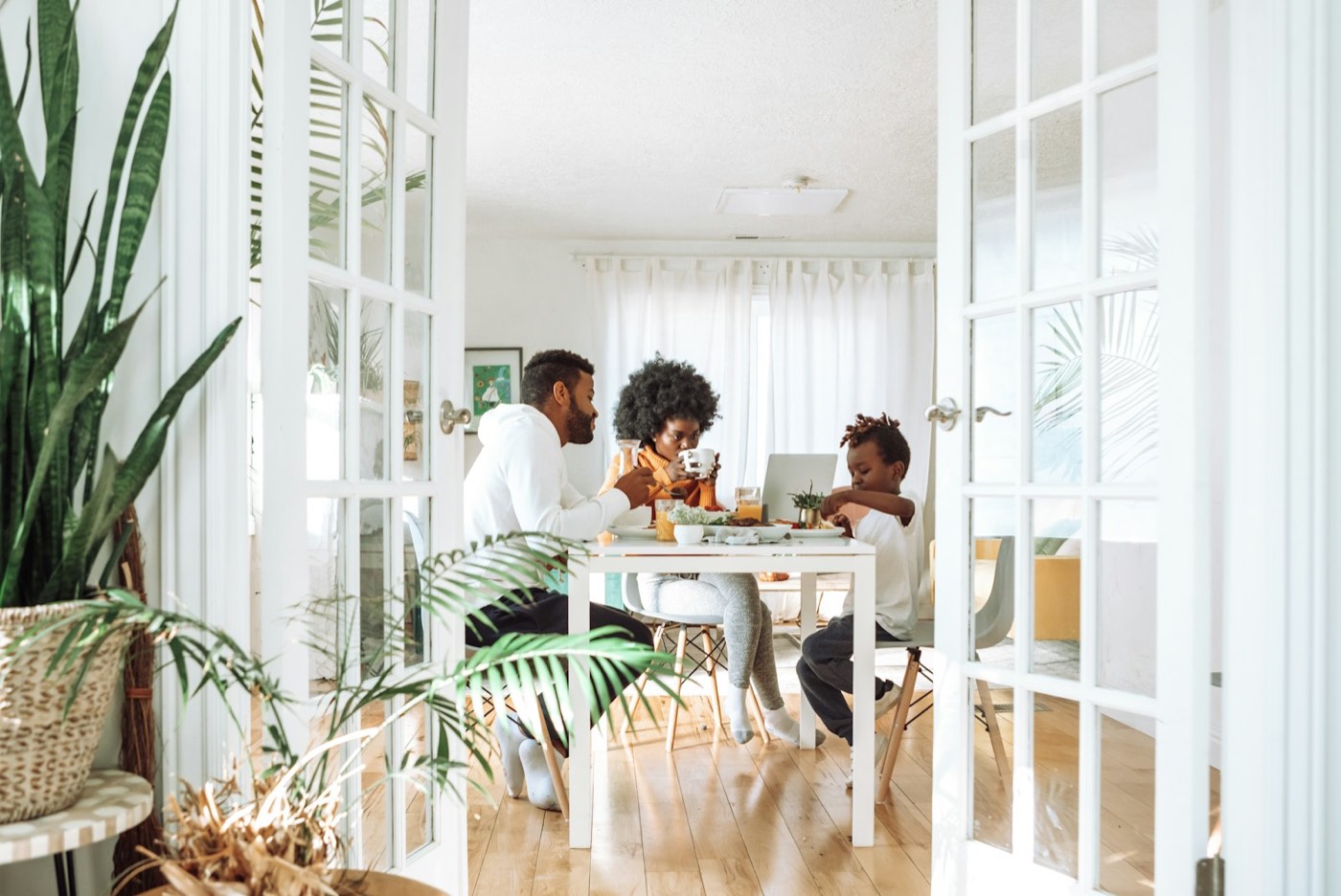 Father, mother and young son eating breakfast together at a white table in a sunny dining room